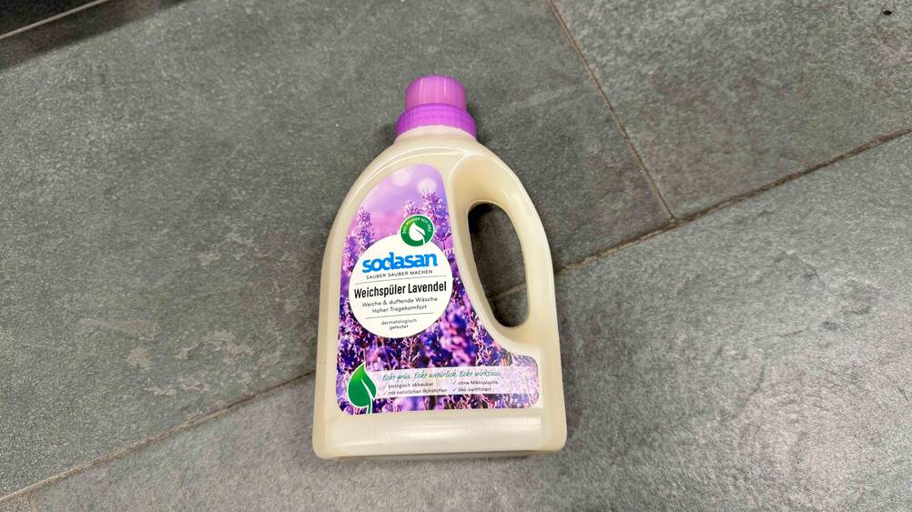 Auf einem grauen Fließenboden befindet sich eine Flasche des getesteten Bio-Weichspülers.