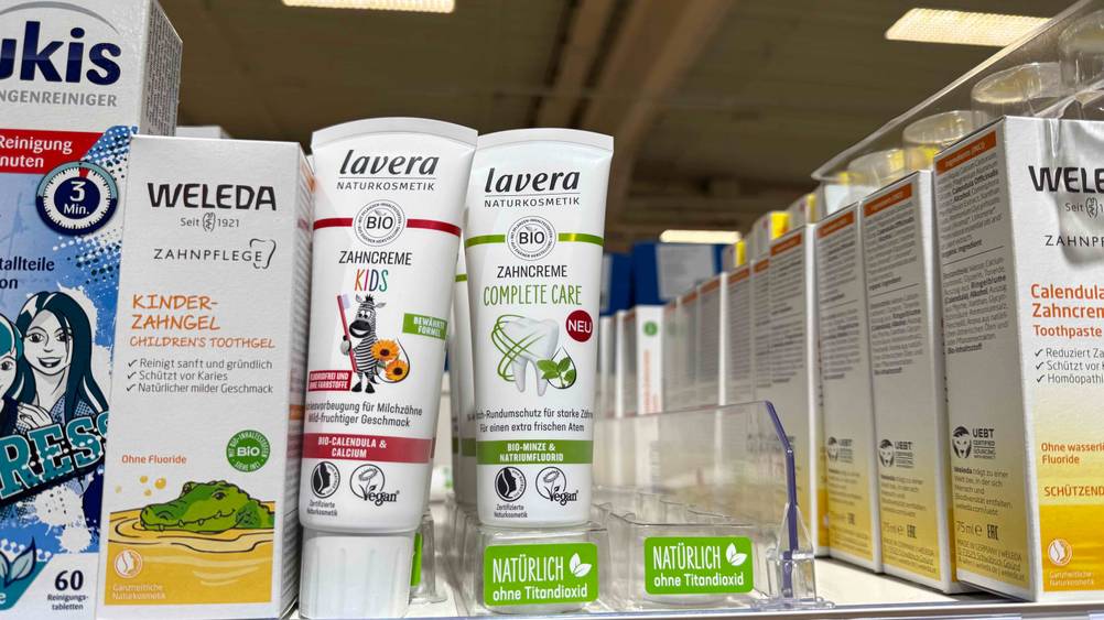 In einem Verkaufsregal stehen mehrere Tuben der Bio-Zahnpasta im Test neben anderen Produkten.