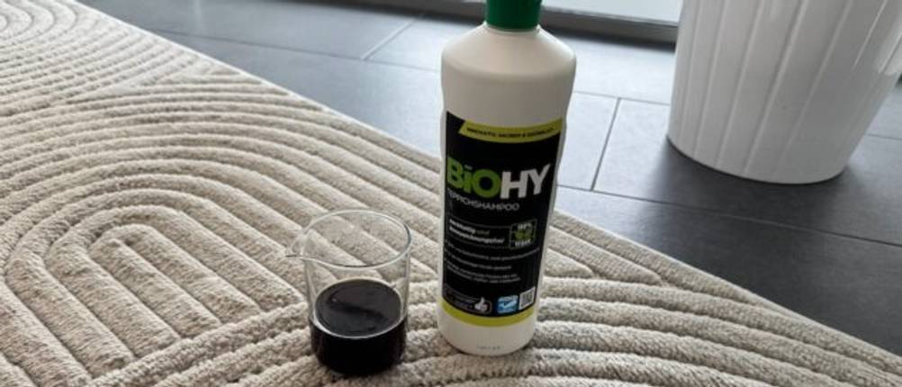 Biohy-Teppich-Shampoo steht auf einem Teppich neben einem Behälter mit Kaffee.