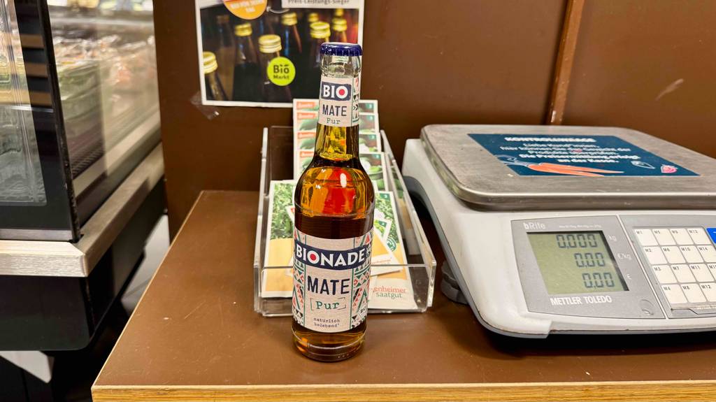 Ein getesteter Bio-Mate Tee in der Flasche steht neben einer Waage in einem Supermarkt.