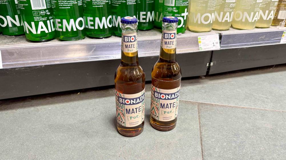 Zwei Flaschen der Bionade im Test stehen vor einem Regal auf dem Boden.