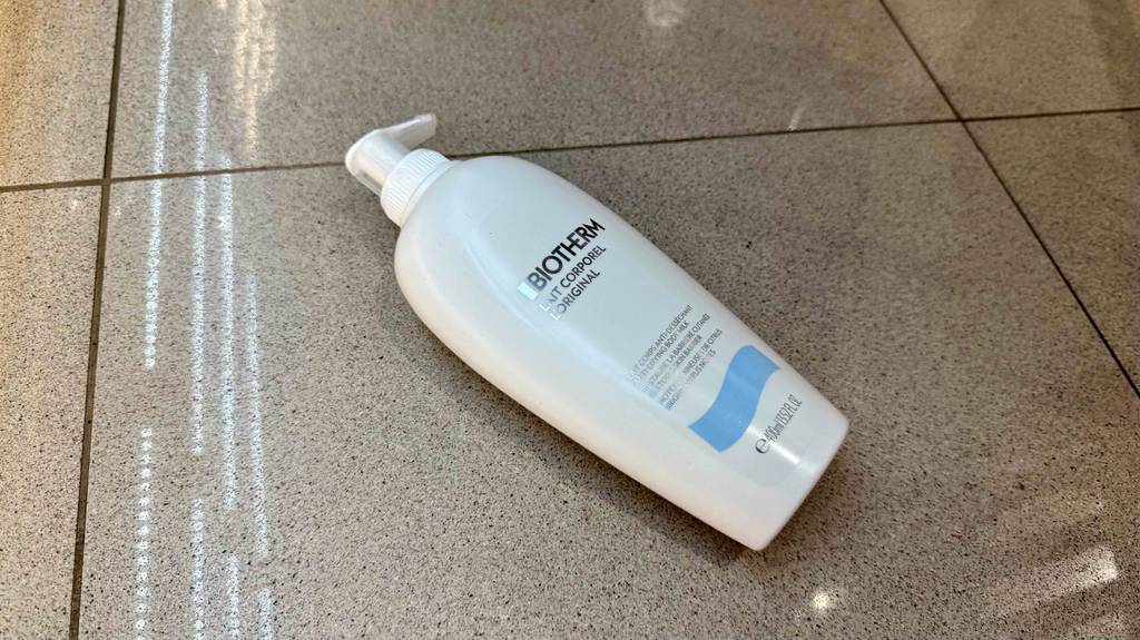 Eine Flasche getestete Biotherm-Bodylotion liegt quer auf einer grauen Fliese.