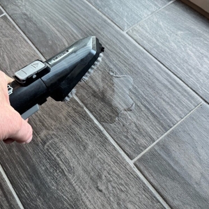Eine Hand hält die Reinigungsbürste des Bissell SpotClean 3689N über den Boden