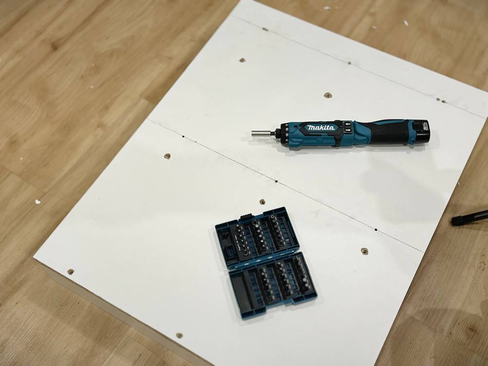 Ein Akkuschrauber und das Bitset von Makita liegen auf einer weißen Spanplatte.