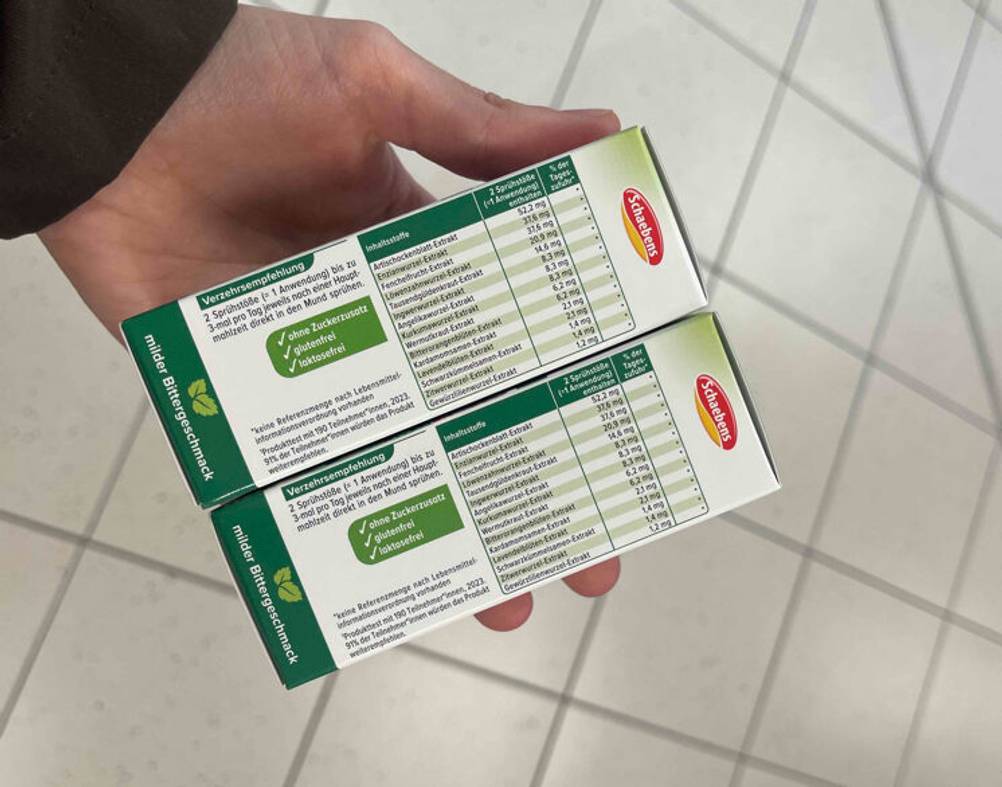 In einer Hand befinden sich zwei Packungen der Bitterstoffe-Tropfen im Test mit Angaben zu den Inhaltsstoffen.