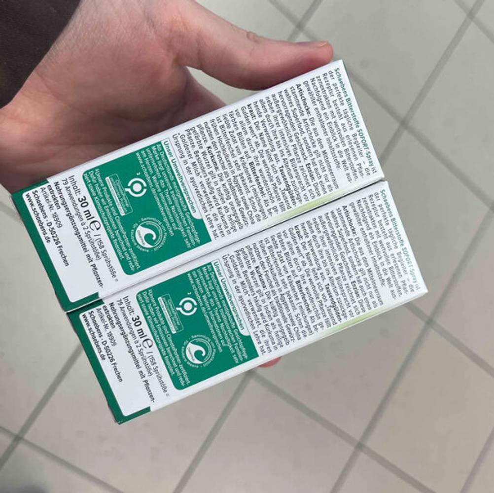 Eine Hand hält zwei Packungen der getesteten Bitterstoffe-Tropfen mit der Rückseite nach oben.