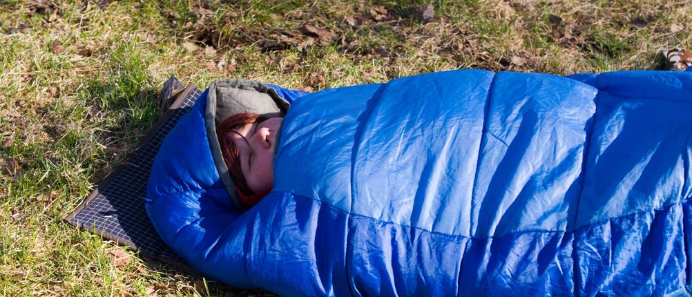 Biwaksack-Test: Eine Frau schläft auf einer Wiese in einem Schlafsack.