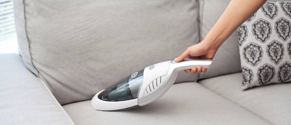 Handstaubsauger von Black und Decker im Test: Eine Hand saugt mit einem weißen Handstaubsauger auf einer hellen Couch.