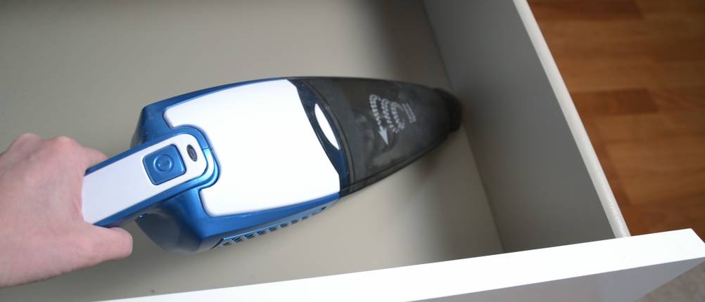Black-und-Decker-Handstaubsauger im Test. Mit einem blau-weißen Handstaubsauger wird eine weiße Schublade gereinigt.
