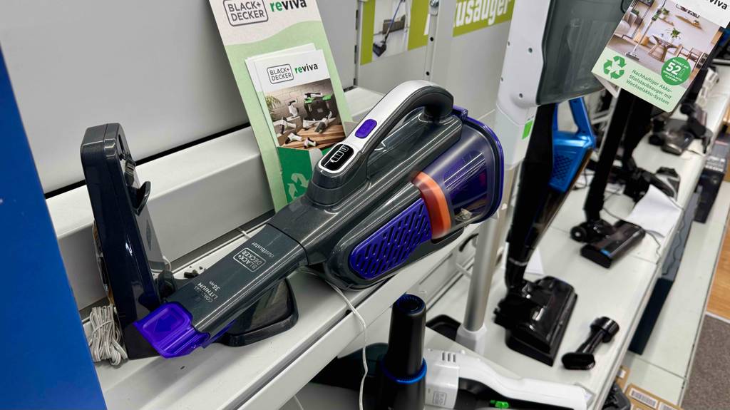Nahaufnahme des batteriebetriebenen Black-und-Decker-Handstaubsaugers im Test, der auf einem Ausstellungsregal neben seiner Ladestation liegt.