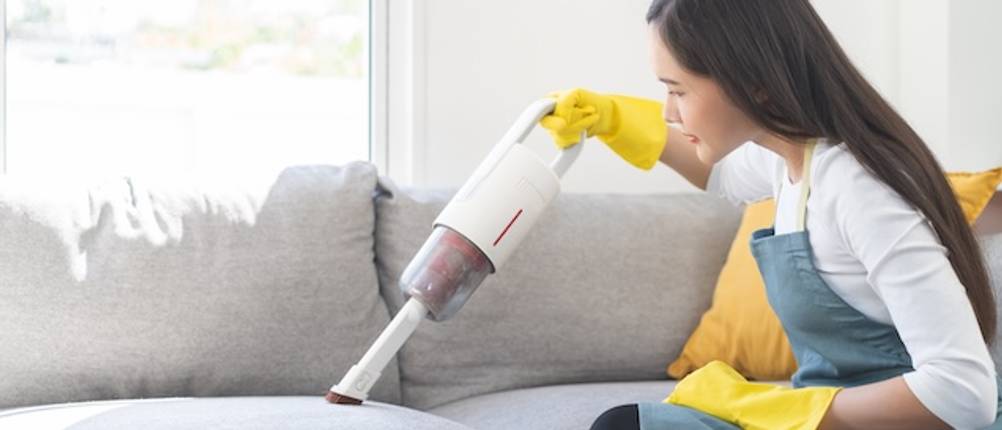 Handstaubsauger von Black und Decker im Test: Eine junge Frau saugt mit einem Handstaubsauger eine helle Couch.