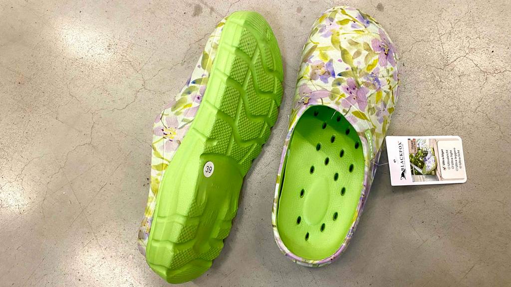 Im Test: Gartenschuhe aus Kunststoff, in Größe 39, im floralen Design, inklusive grüner, gelöcherter Innensohle sowie grüner Profilsohle, befinden sich auf einem grauen Zementboden.