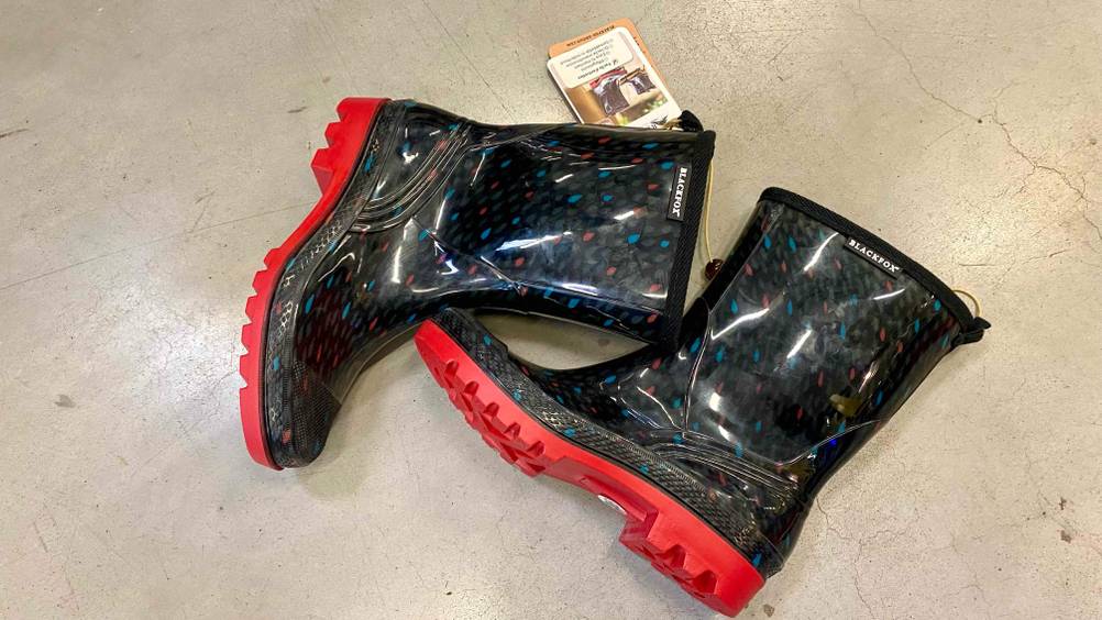 Gummistiefel-Damen-Test: Ein schwarz-bunt gemustertes Paar Gummistiefel mit roten Sohlen liegt auf einem grauen Betonboden.
