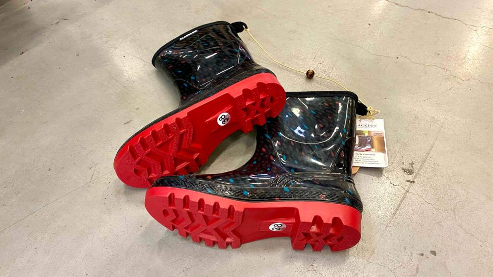 Gummistiefel-Damen-Test: Ein Paar schwarz-bunt gemusterte Gummistiefel für Damen mit der roten Sohle nach vorne auf der Seite liegend.