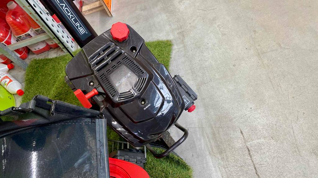 Ansicht von oben auf eine schwarze Motorhacke im Test, die sich in einem Ausstellungsbereich neben Garten-Utensilien befindet.