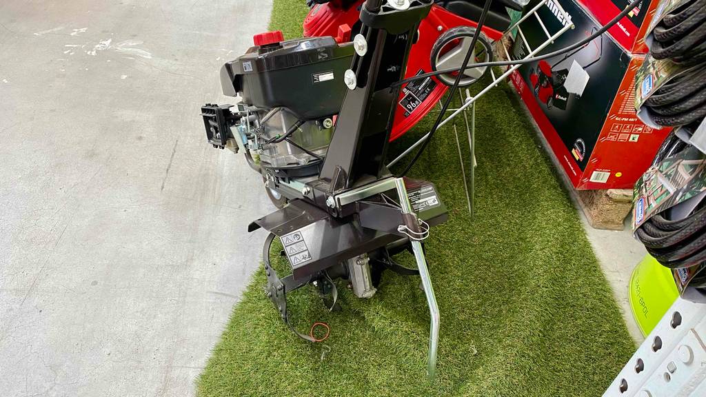Motorhacken im Test: Detailansicht von hinten auf ein schwarzes Modell, das in einem Gartencenter-Ausstellungsbereich neben weiteren Garten-Utensilien steht.