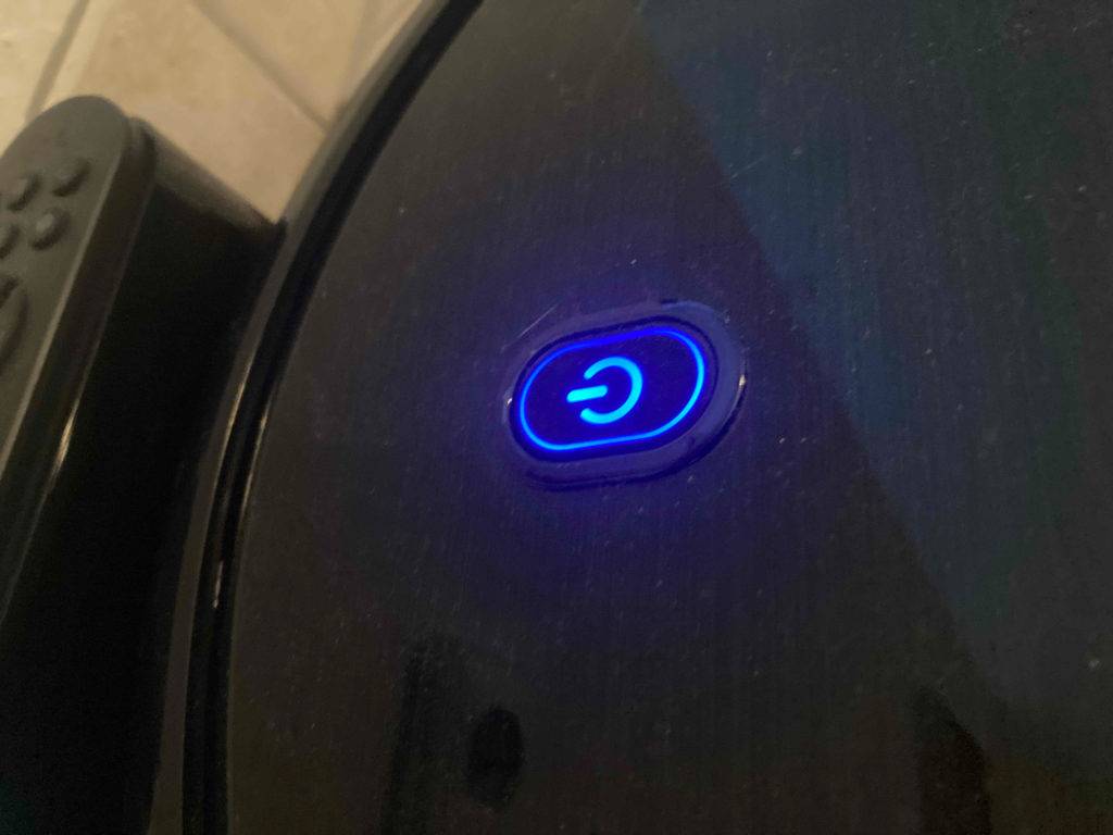 Detailansicht des blau leuchtenden Einschaltknopfes auf einem schwarzen Eufy-Saugrobotor im Test.