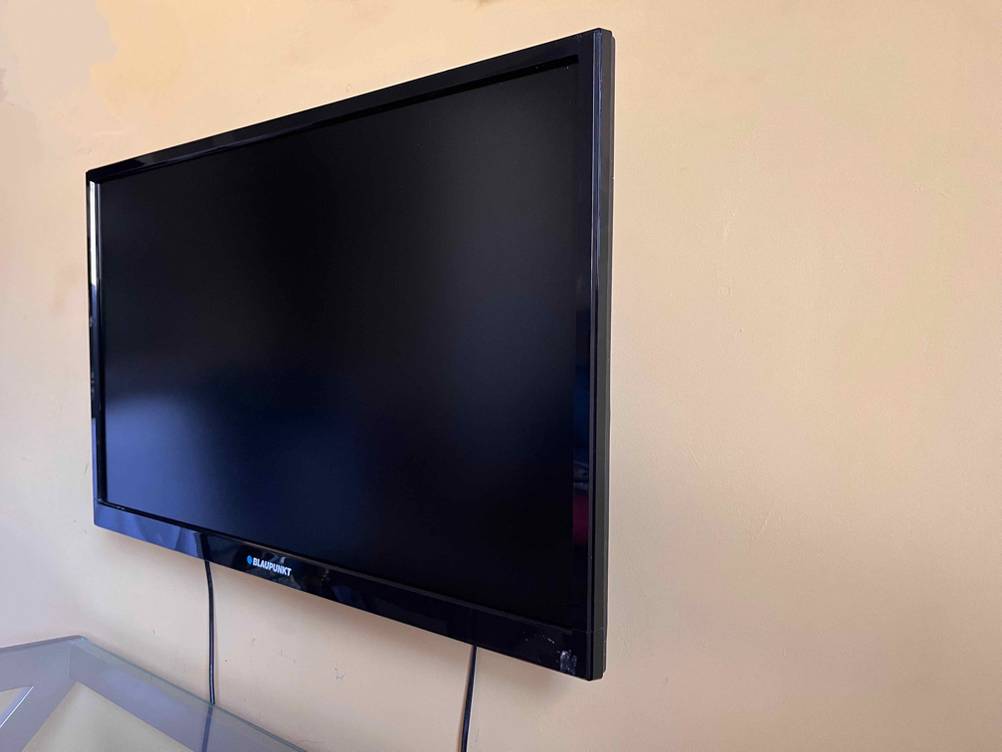 Ein an der Wand hängender, schwarzer Fernseher von der Seite betrachtet.
