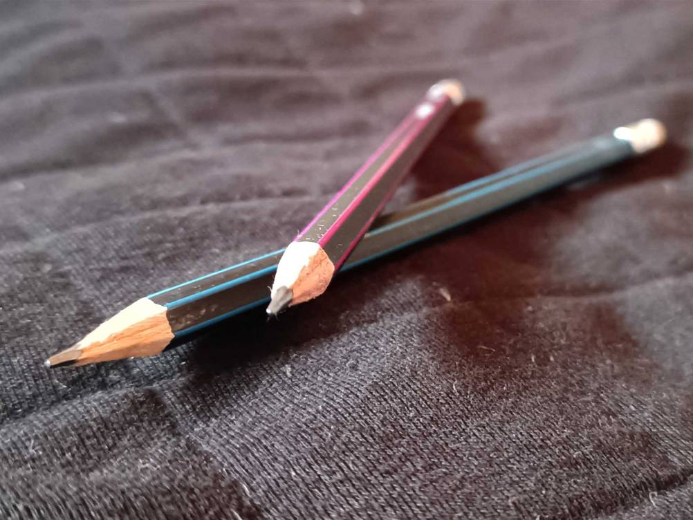 Zwei Bleistifte im Test übereinander von vorne auf einem dunklen Stoff.