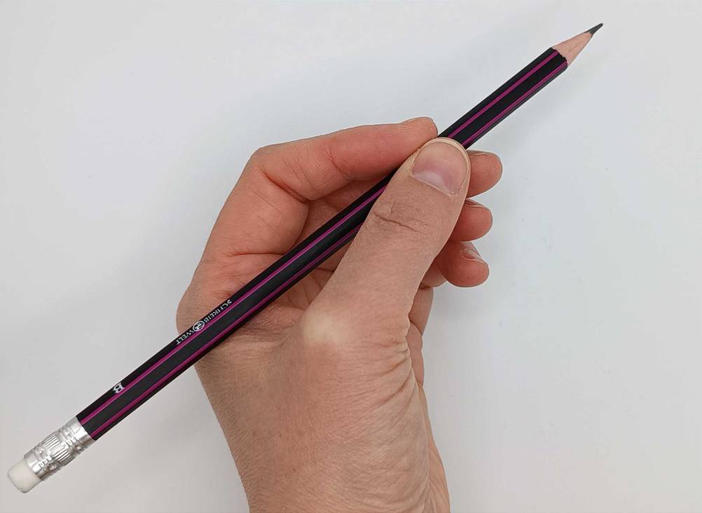 Eine Hand hält einen getesteten Bleistift vor eine hellen Wand.