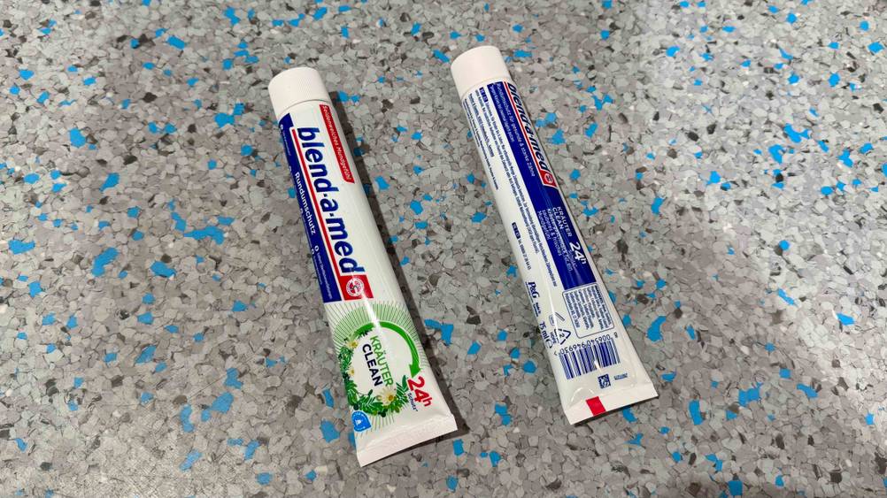 Blend-a-med-Zahnpasta im Test: Zwei Tuben auf dem Boden liegend, eine mit der Vorderseite nach oben, eine mit der Rückseite.