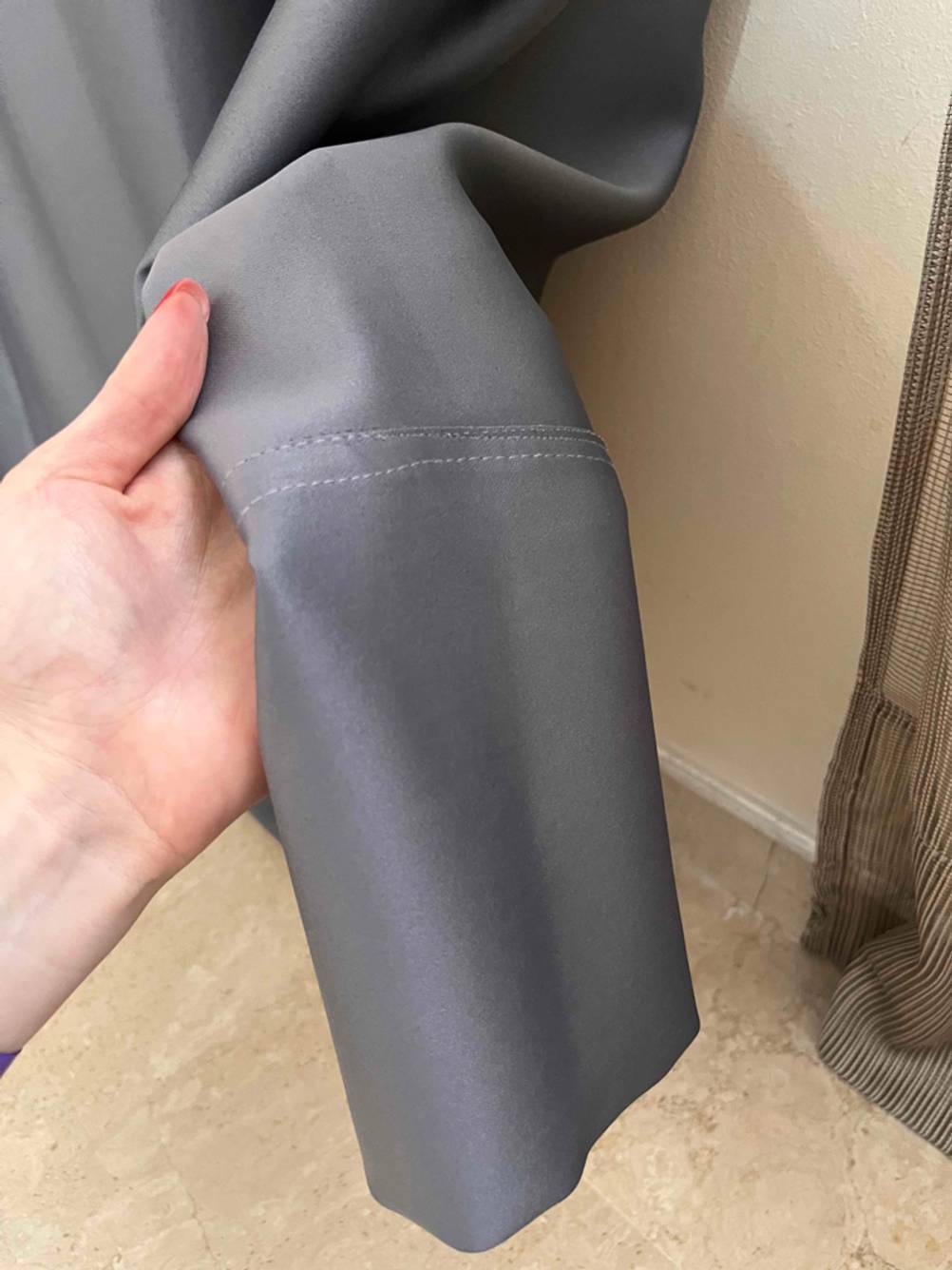 Im Test: Nahaufnahme des unteren Saumes eines blickdichten Vorhangs den eine Hand hält.