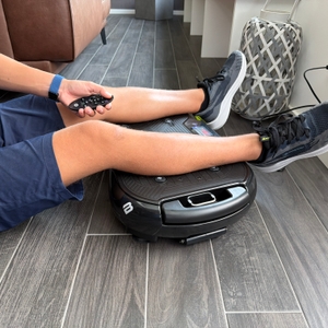 Eine Hand steuert die Bluefin Ultra Slim Plus mit einer Fernbedienung, während die Beine auf der Fläche liegen.