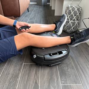 Eine Hand steuert die Bluefin Ultra Slim Plus mit einer Fernbedienung, während die Beine auf der Fläche liegen.