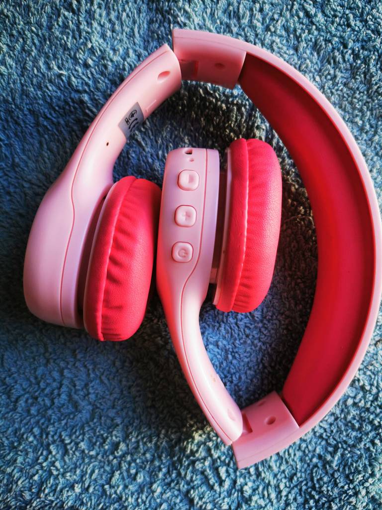 Der pinkfarbene Bluetooth-Kopfhörer bis 50 Euro im Test liegt auf einem blauen Stoff.