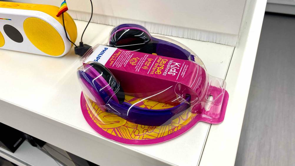 Getestet: Verpackte Bluetooth-Kopfhörer für Kinder auf einem weißen Regal neben anderen Produkten.