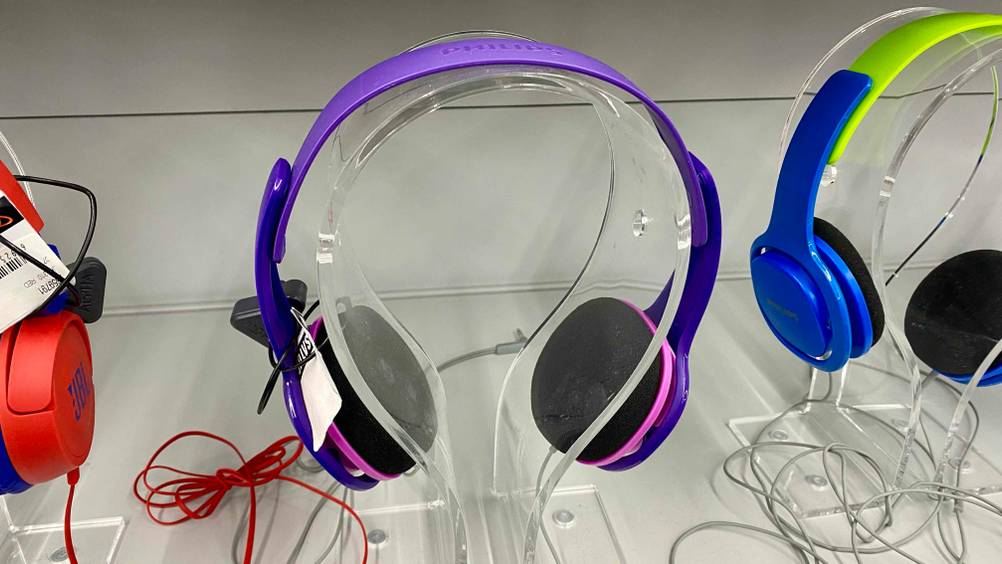 Bluetooth-Kopfhörer für Kinder getestet: Ein Paar Kopfhörer in rosa-lila auf einem transparenten Gestell in einem Verkaufsregal.