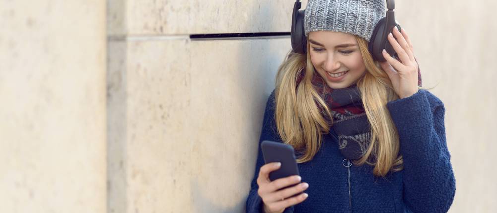 bluetooth-muetze-test: Frau mit Pudelmütze und Kopfhörern schaut auf ihr Smartphone