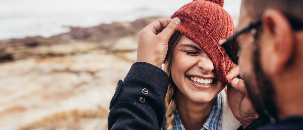 bluetooth-muetze-test: Mann zieht an der roten Mütze einer Frau, die schief über dem Gesicht hängt.