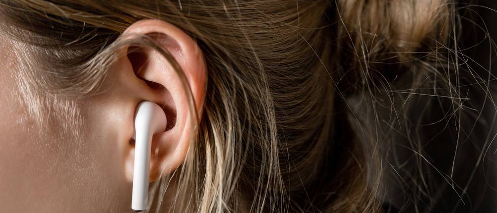 bluetooth-muetze-test: Nahaufnahme eines Frauenohrs mit weißem In-Ear-Kopfhörer