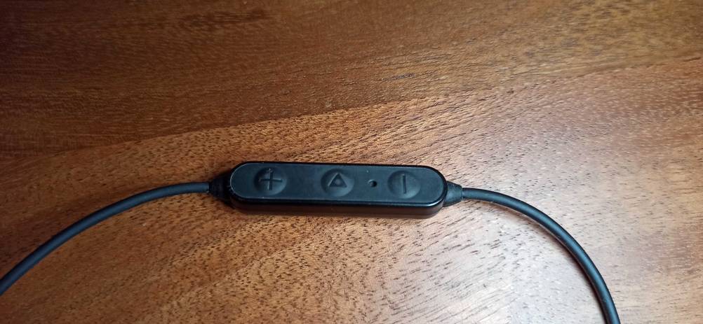 Nahaufnahme der Bedienelemente eines Bluetooth-Sportkopfhörer im Test auf einer Holzfläche.