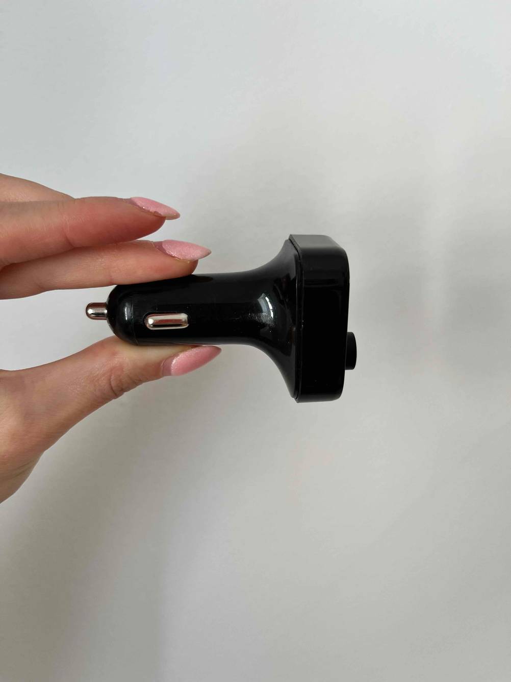 Im Test: Hand hält ein Bluetooth Autoradio für den Zigarettenanzünder seitlich vor weißer Wand.
