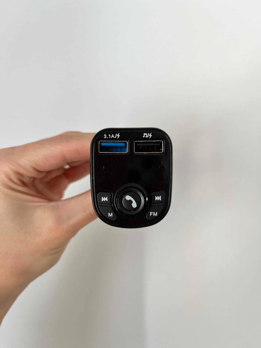 Im Test: Hand hält ein Bluetooth Autoradio vor weißer Wand.