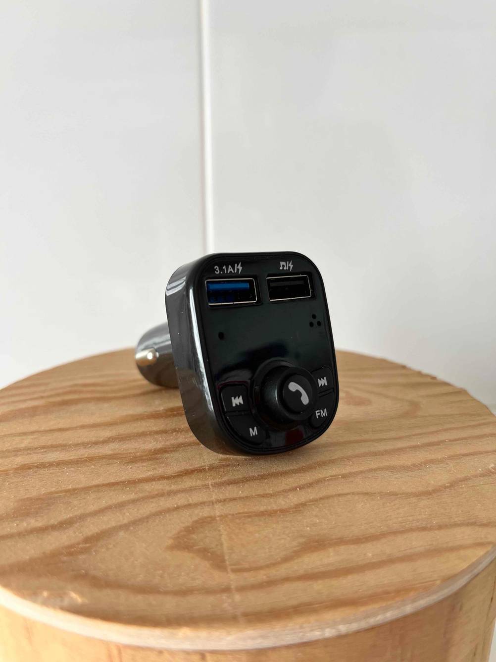 Im Test: Bluetooth Autoradio für Zigarettenanzünder liegt auf rundem Holztisch.