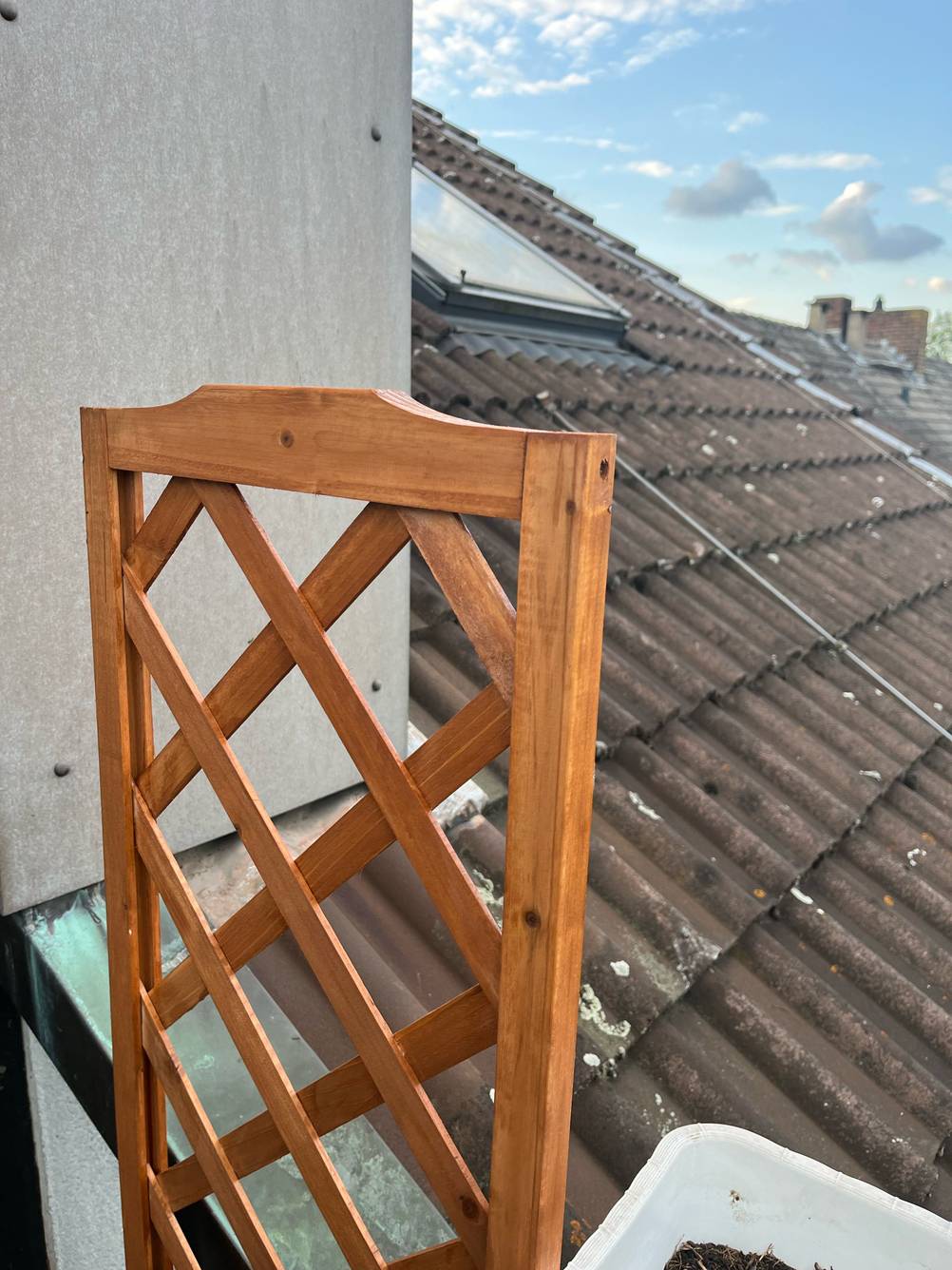 Nahaufnahme des Ende des Rankgitters eines Blumenkasten mit Rankgitter im Test auf einem Balkon im Hintergrund ein Dach.