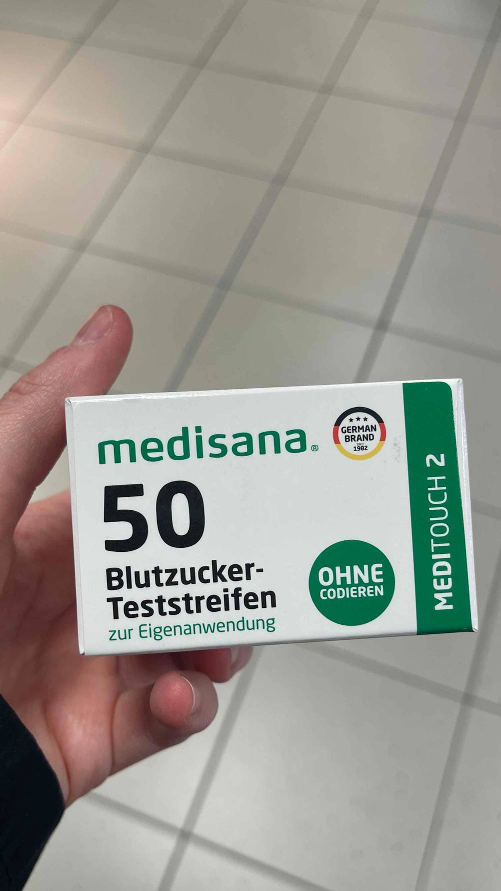 Eine Hand hält die Packung der getesteten Blutzuckerteststeifen.