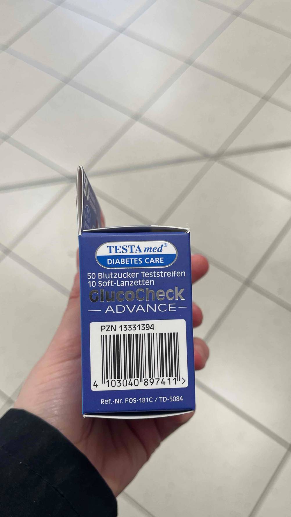 Seitenansicht der Verpackung mit Strichcode der Blutzuckerteststeifen im Test von einer Hand gehalten.
