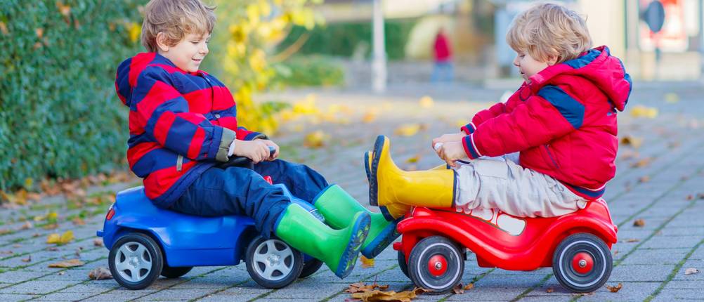 Bobby-Cars im Test: Zwei Kinder die mit Bobby-Cars draußen herumfahren. Ein rotes und ein blaues Bobby-Car sind zu sehen.