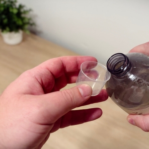 Eine Hand hält eine Dosierkappe, die andere Hand hält die gekippte Flasche an den Rand der Dosierkappe.