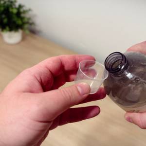 Eine Hand hält eine Dosierkappe, die andere Hand hält die gekippte Flasche an den Rand der Dosierkappe.