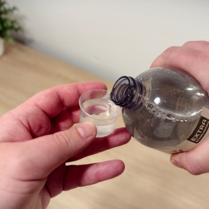 Eine Hand hält eine Dosierkappe, die andere Hand hält die Flüssigkeit in die Dosierkappe kippt.