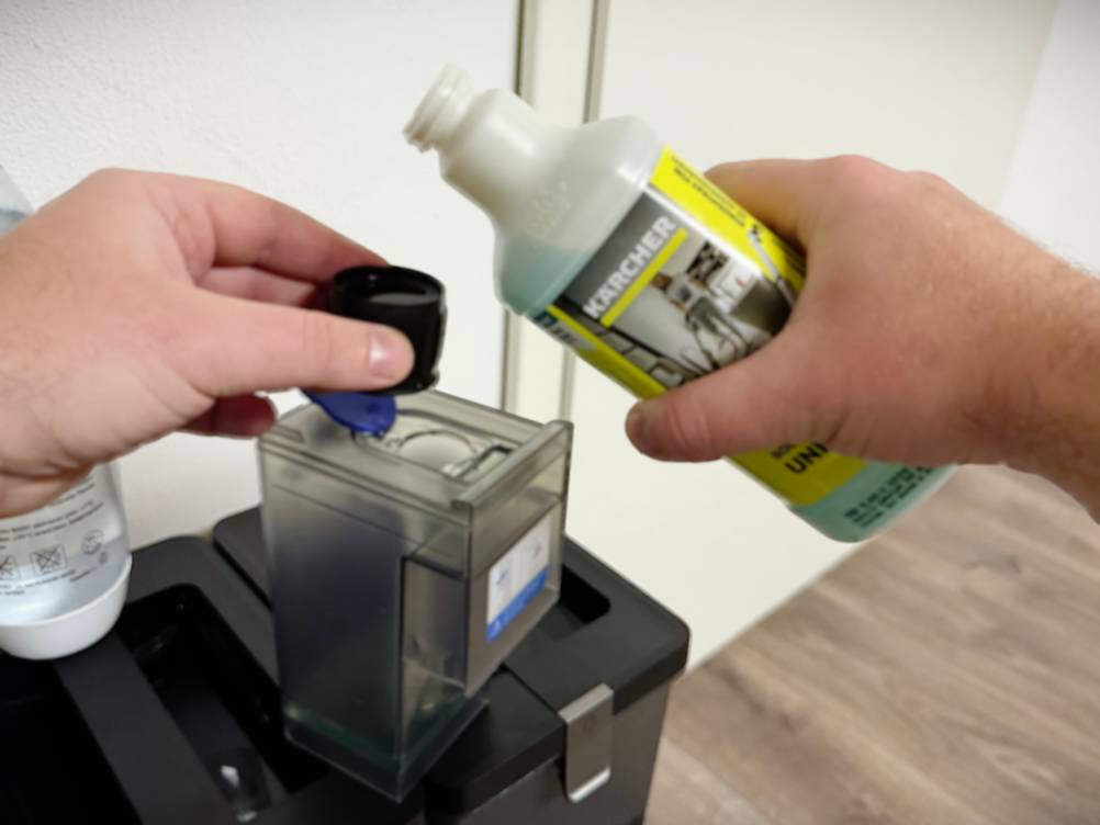 Eine Hand hält die Dosierkappe während die andere Hand den Bodenreiniger von Kärcher hält.
