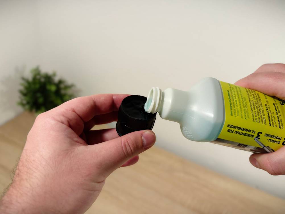 Eine Hand hält eine Dosierkappe während der Kärcher-Bodenreiniger hinein gekippt wird.