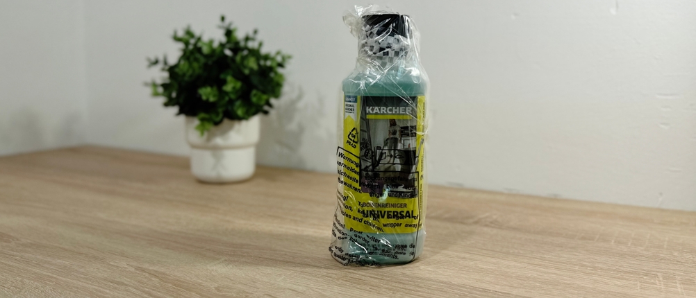 Der Kärcher-Bodenreiniger mit Plastikverpackung steht auf einer hölzernen Platte vor einem weißen Hintergrund und einer Topfpflanze.