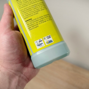 Eine Hand hält den Bodenreiniger von Kärcher vor einem weißen Hintergrund und einer hölzernen Platte. 