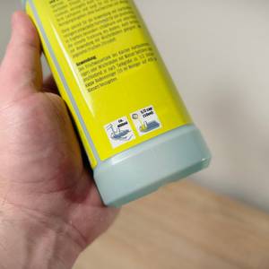 Eine Hand hält den Bodenreiniger von Kärcher vor einem weißen Hintergrund und einer hölzernen Platte. 